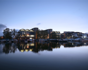 Campus in the early evening, as seen from across the Brayford Pool, with the buildings reflecting in the still water