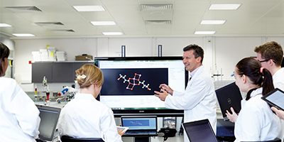 Academic in white lab coat showing students a chemical model on a screen