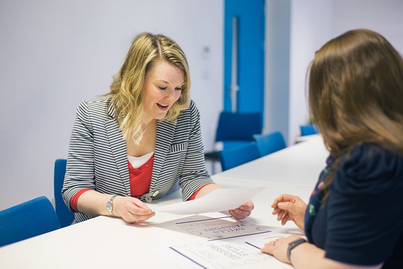 Female member of staff sat opposite another woman, in conversation