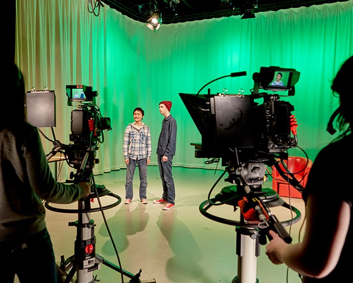 A TV studio with cameras and actors in front of a green screen