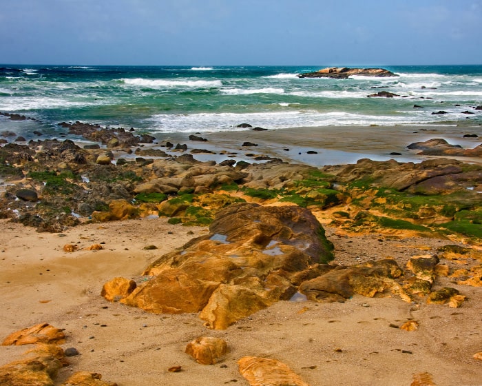 Sandy beach with large brown rocks, and the sea in the distance