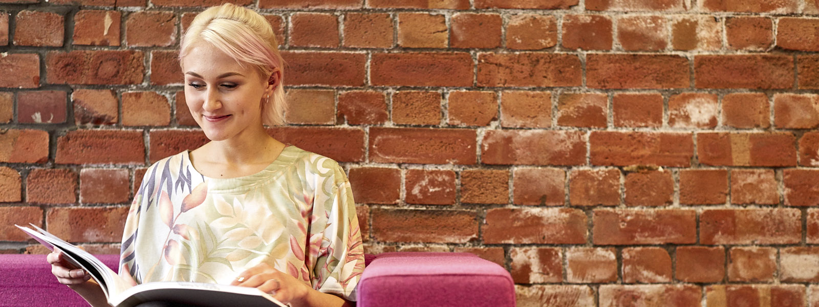 Female student sat reading a book on a sofa