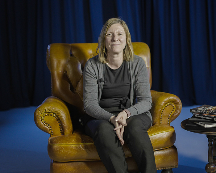 A woman sat in an armchair next to a table of books smiling