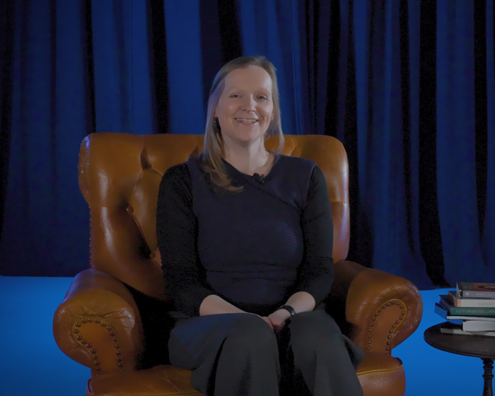 A woman sat in an armchair next to a table of books smiling