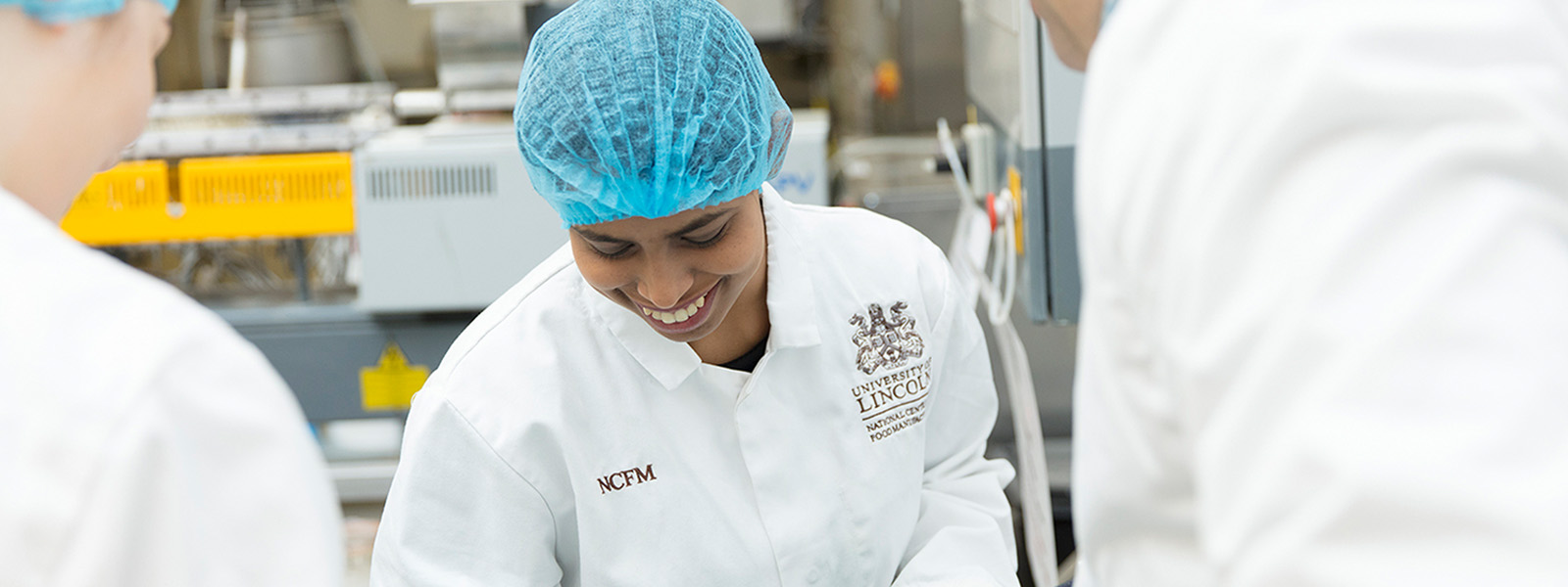 A student in a lab coat and hairnet working in a lab