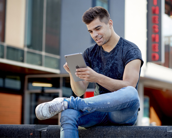 A student sitting outside on campus working on a tablet