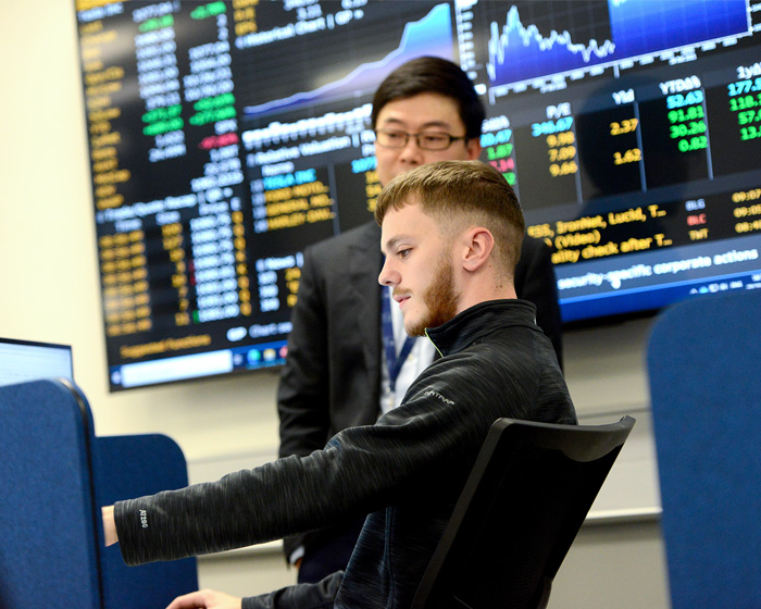 A student and mentor looking at a screen with stock exchange information behind them